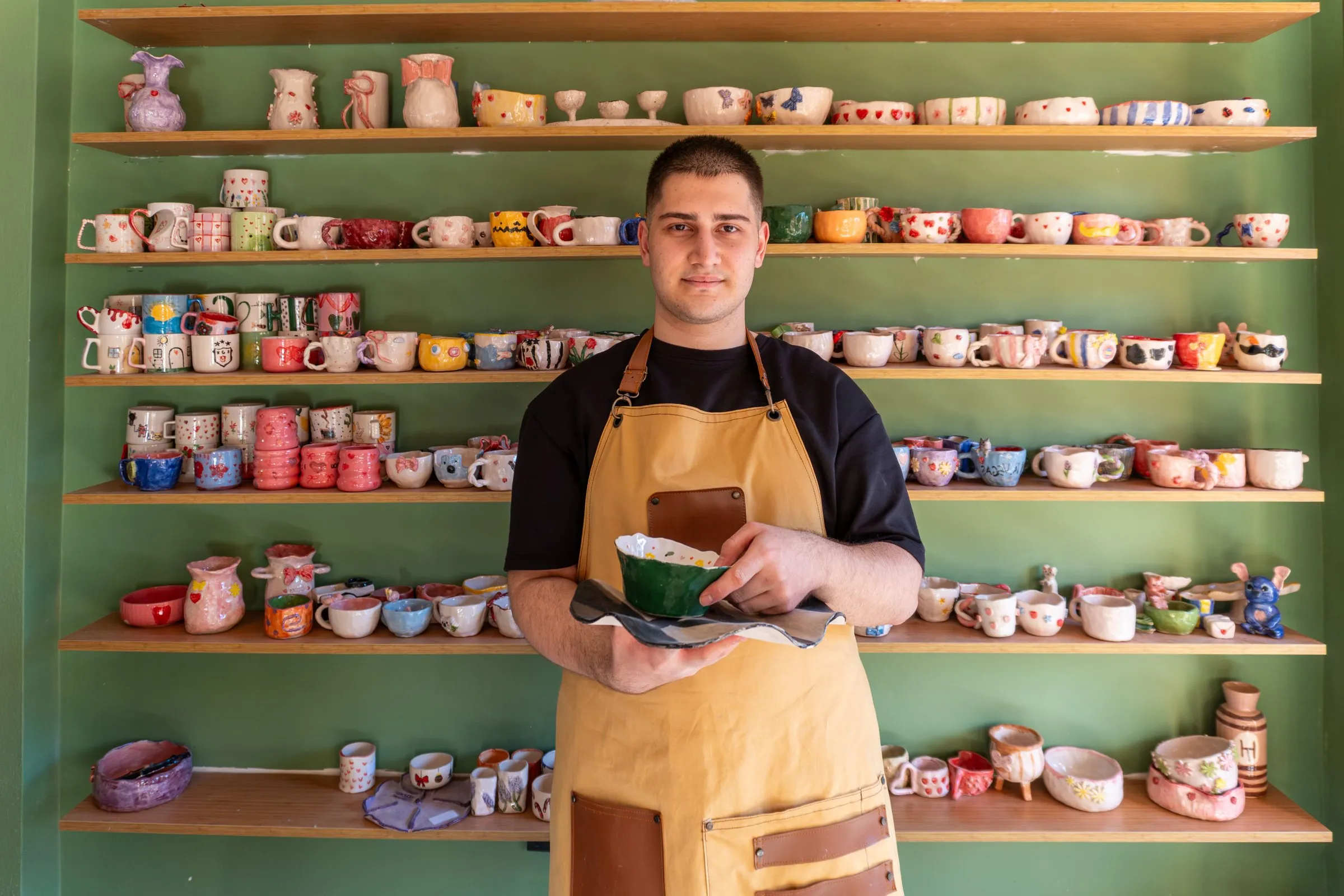 Artisan céramiste dans sa boutique, devant des étagères de tasses