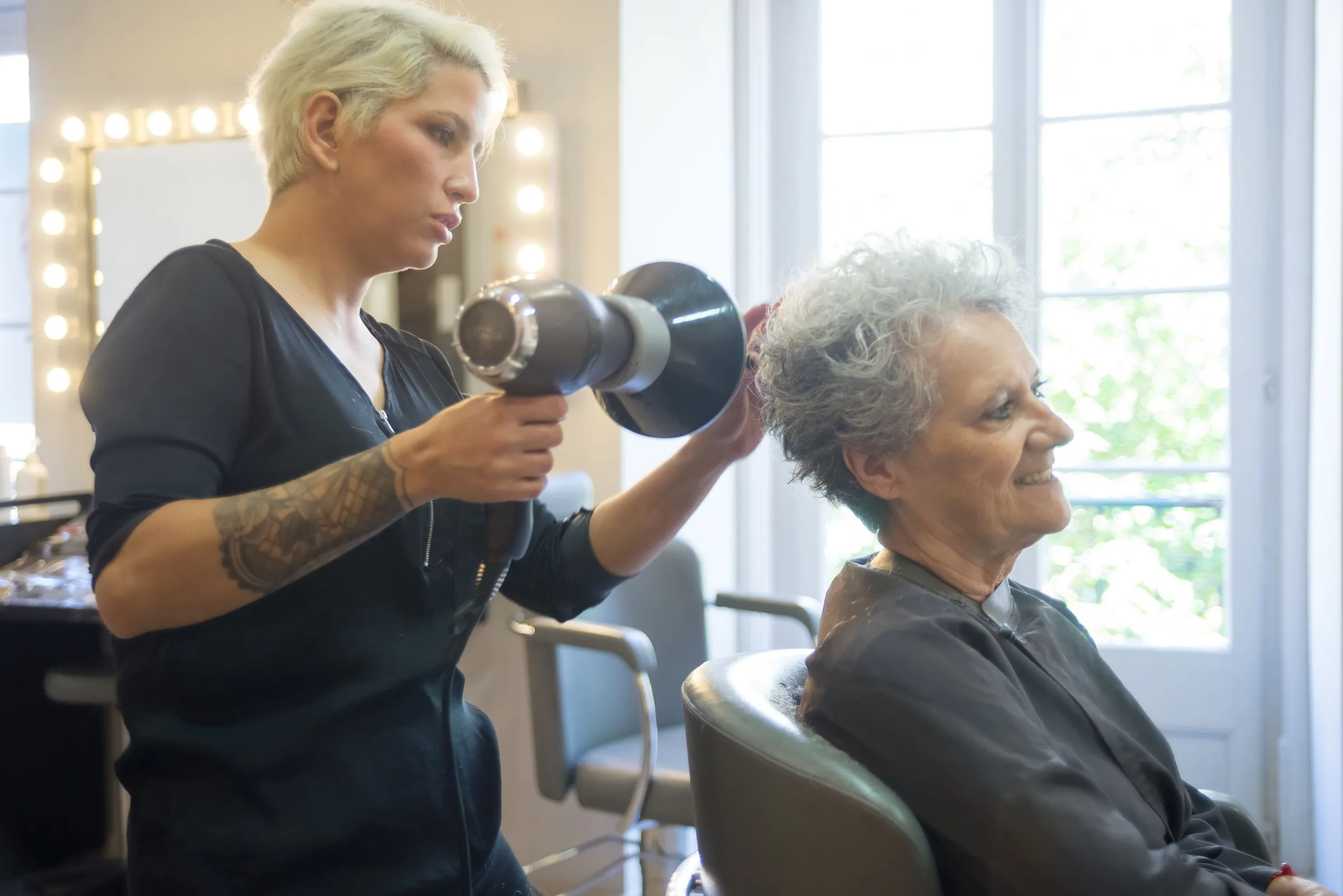 Coiffeuse qui sèche les cheveux d'une cliente dans son salon