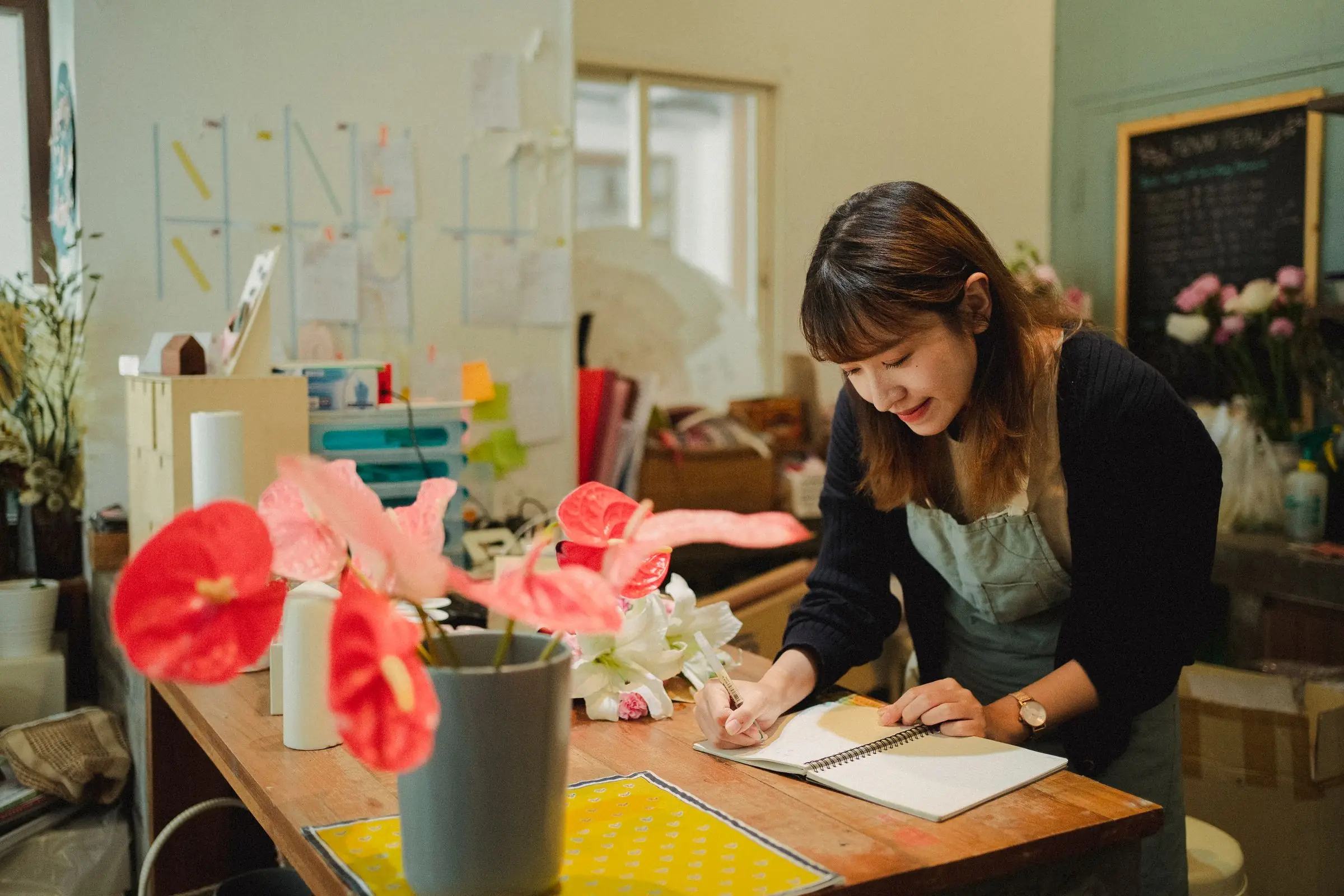 Florist writing in a notebook at her shop's worktable