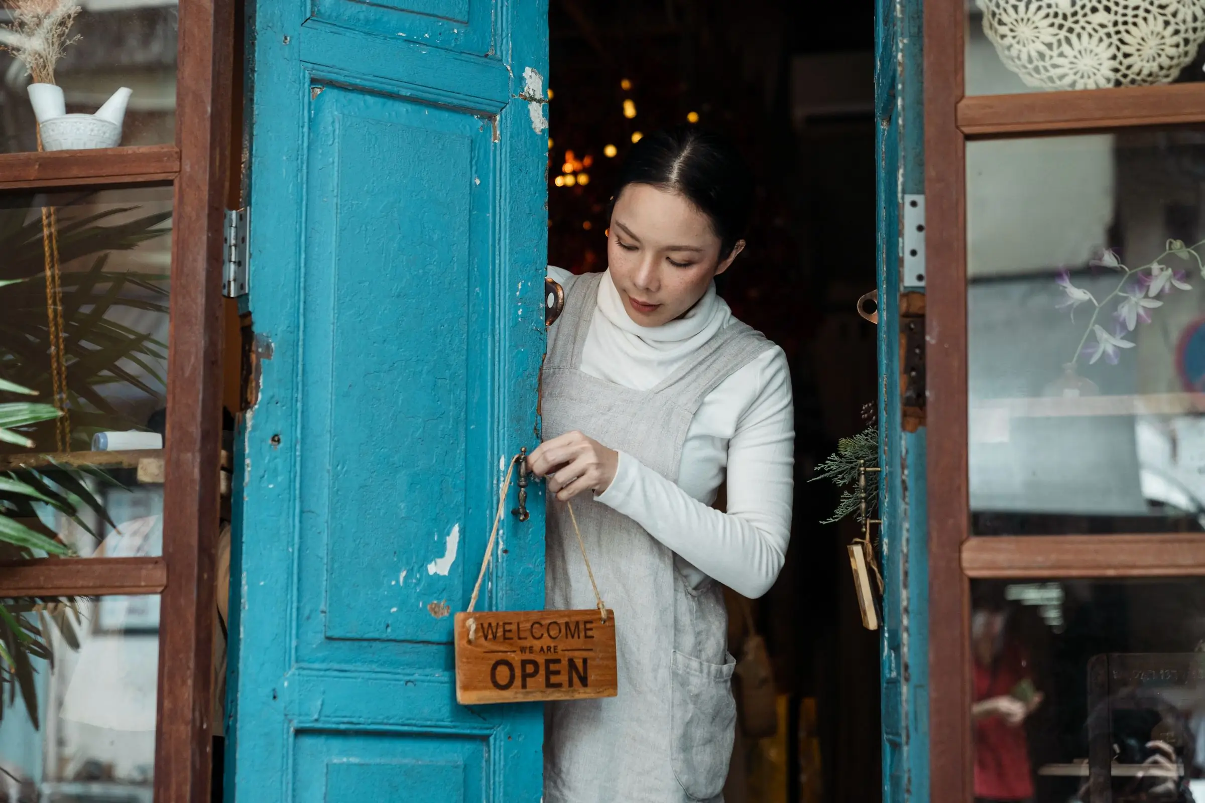 Commerçante qui accroche l'affiche « ouvert » à la porte de son café