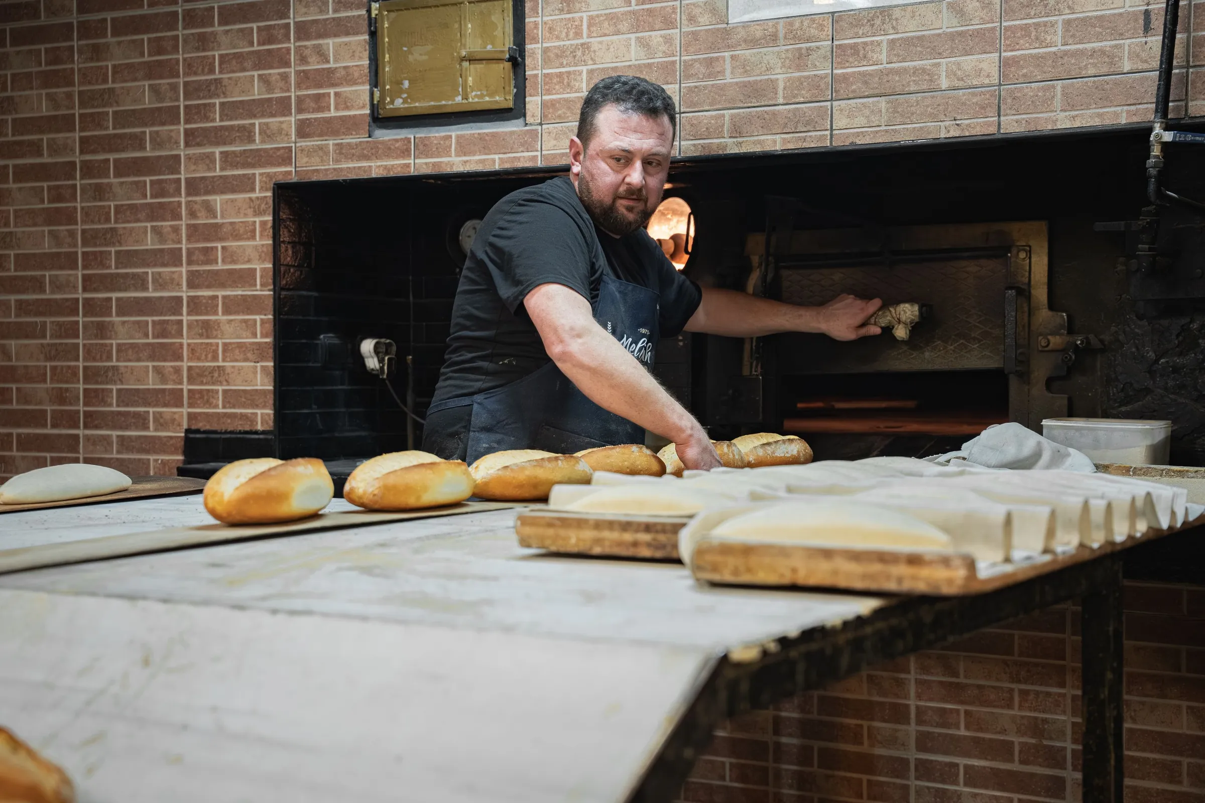 Baker at work in front of the bread oven, loaves on the table